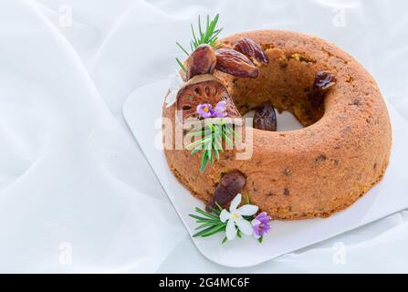Date Cake and Decorate  with dried dates. dried quince and rosemary leaves on white cloth background, healthy cake concept Stock Photo