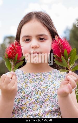 Portrait of a little child outdoors. She is holding a flower in each of her hands. Stock Photo