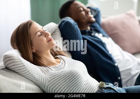 Relaxing Concept. Young Interracial Couple Resting Together On Comfortable Sofa At Home Stock Photo