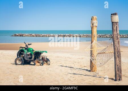 Vintage green ATV on the sandy beach. Quad ATV all terrain vehicle parked on beach, Motor bikes ready for action with summer sun flaring on bright day Stock Photo