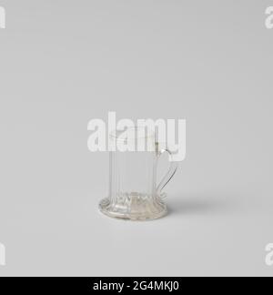 Cup with ear, body cylindrical with vertical ridges. Cup of bright colorless glass, cylindrical of shape, vertically ribbed, with widened bottomed soil, and arranged ear ending in curl. Stock Photo