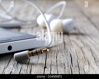 closeup of unplugged earphones mini-jack smartphone connector on wooden board, macro, shallow depth of field Stock Photo