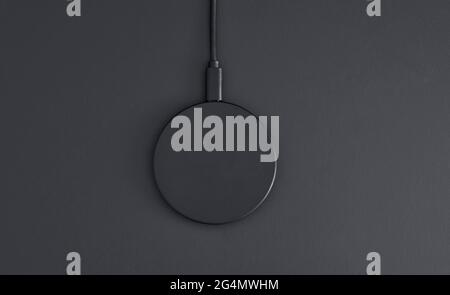 High angle view of black plastic circular wireless charger laying on dark grey desk. Modern technology, wireless device and transfer of energy concept Stock Photo
