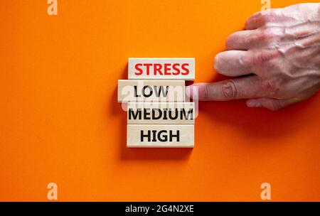 Low or high stress level symbol. Businessman chooses the wooden block with words low stress. Words stress low medium high. Beautiful orange background Stock Photo