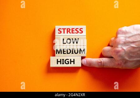 Low or high stress level symbol. Businessman chooses the wooden block with words high stress. Words stress low medium high. Beautiful orange backgroun Stock Photo