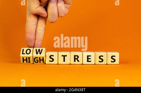 Low or high stress level symbol. Businessman turns wooden cubes and changes words high stress to low stress. Beautiful orange background. Low or high Stock Photo