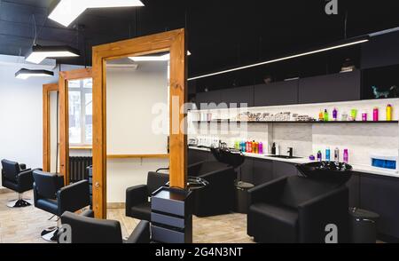 Beauty salon barbershop interior. Large wood-framed mirrors and comfortable black leather armchairs in a modern, cozy and bright space. Stock Photo