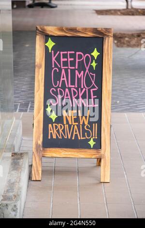 Blackboard sandwich board sign  on sidewalk outside clothing store in neon colors announcing new arrivals - Selective focus Stock Photo