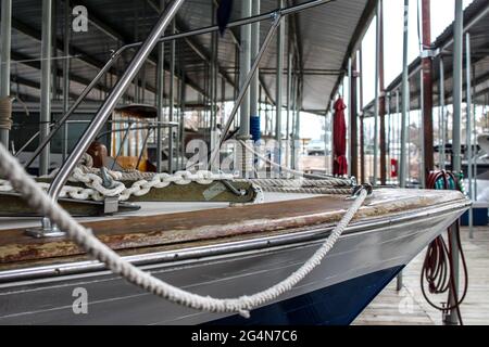 Close-up of bow of old rustic wooden boat with ropes and chains - shallow focus with other boats on covered dock blurred behind Stock Photo