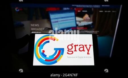 Person holding smartphone with logo of US broadcasting company Gray Television Inc. on screen in front of website. Focus on phone display.
