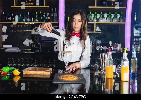 Busy female with bottle of beer sitting on couch and browsing netbook near male flatmate scrolling Internet on cellphone on terrace under blue sky Stock Photo