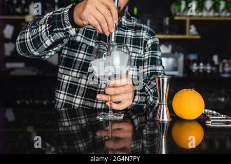 Cropped unrecognizable barman is preparing an alcoholic drink in glass with ice cubes in a night club Stock Photo