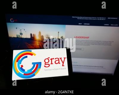 Person holding cellphone with logo of US broadcasting company Gray Television Inc. on screen in front of business web page. Focus on phone display. Stock Photo
