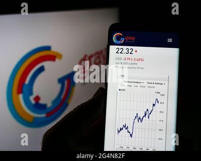 Person holding cellphone with webpage of US broadcasting company Gray Television Inc. on screen in front of logo. Focus on center of phone display.