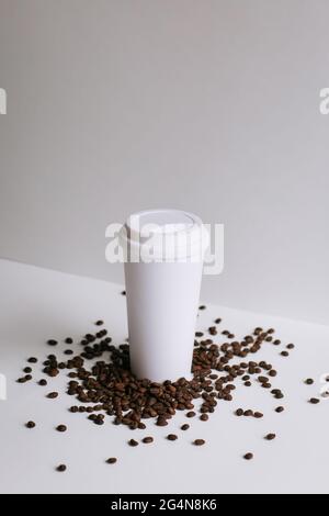 High angle of takeaway paper cup placed on white table with scattered coffee grains in studio Stock Photo