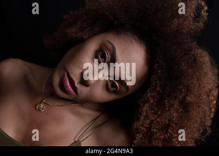 Charming African American female model with curly hair looking at camera in dark studio Stock Photo