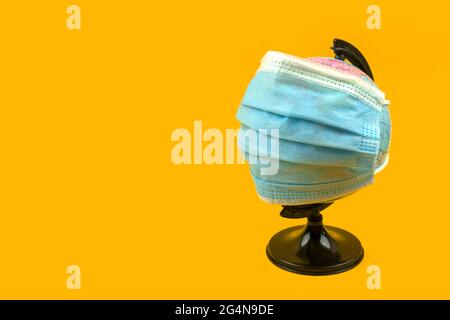 COVID-19 back to school creative background, the globe with medical mask on a orange background, copy space photo Stock Photo