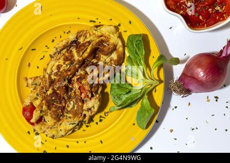 Delicious omelette with chopped parsley on plate against sun dried tomatoes and raw red onion on white background Stock Photo