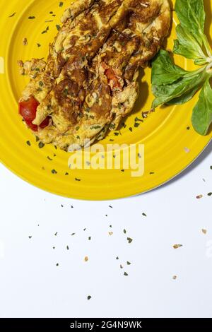 Delicious omelette with chopped parsley on plate against sun dried tomatoes on white background Stock Photo