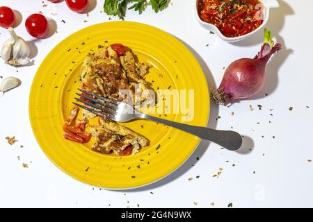 Delicious omelette with chopped parsley on plate against sun dried tomatoes and raw red onion on white background Stock Photo