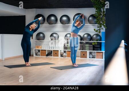 Full body of young female with instructor standing in Upward Salute Side  Bend pose while practicing yoga together in modern fitness studio Stock  Photo - Alamy
