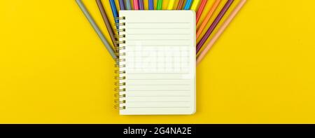 Banner back to school template with lined notebook and color drawing pencils, yellow table background, top view Stock Photo
