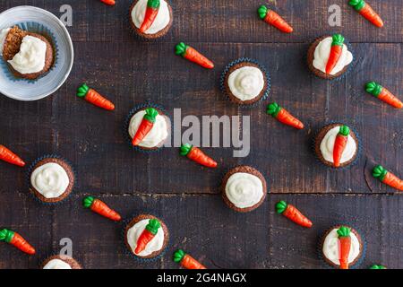Seamless pattern of composed decorative sweet carrots and cupcakes with cream on wooden background Stock Photo