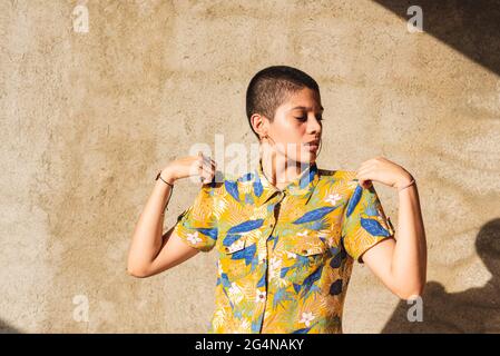 Young bisexual ethnic female with short hair in earrings on beige background with shadows Stock Photo