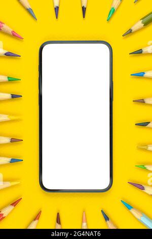 School flat lay workspace mockup with modern smartphone, copy space and blank white screen, yellow desktop with color pencils, top view Stock Photo