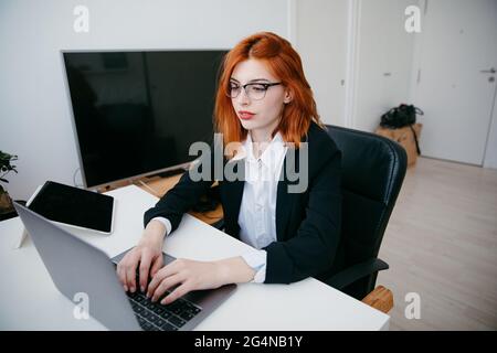 Young female entrepreneur working on netbook at desk with tablet and smartphone at home Stock Photo