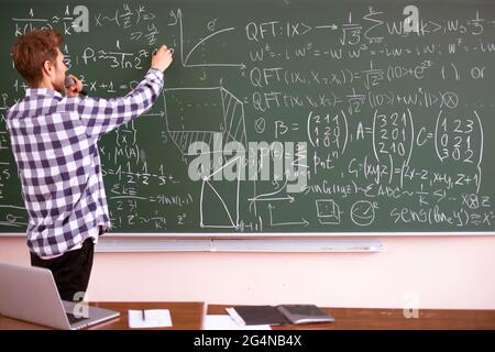 teacher of young professor explains the law of physics for students on the lesson, standing near the blackboard Stock Photo