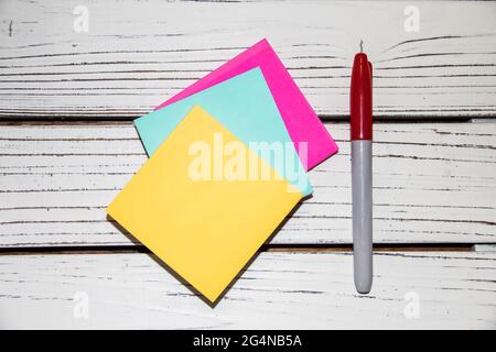 Colorful pink and blue and yellow stick on notes and a market on a white board background - flat lay Stock Photo