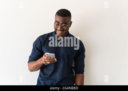 African American adult male in stylish outfit and eyeglasses standing with netbook in hands while using cellphone on white background Stock Photo