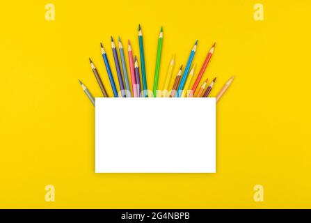 Creative school mockup with blank white paper and color school pencils on desktop, yellow background, copy space and top view Stock Photo
