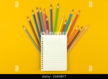 Back to school template or mockup, notepad with color drawing pencils on the yellow desktop background, top view Stock Photo