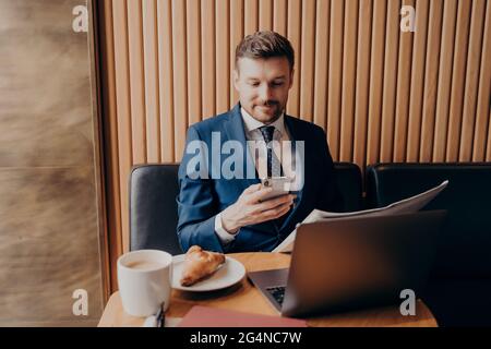 Confident young businessman in formal clothes enjoying coffee and working remotely in cafe Stock Photo