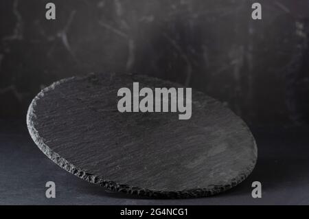 Round stone tray. Black slate tray. Empty slate tray. Stand for food and snacks. Tilted podium. Stock Photo