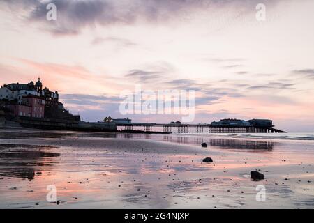 Colourful reflections of Cromer pier seen in the wet sand at low tide during dusk one evening in June 2021 on the North Norfolk coast. Stock Photo