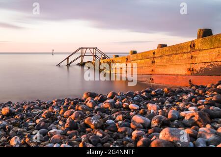 A long exposure of the golden light at sunset falling onto a groyne at Cromer beach on the North Norfolk coast. Stock Photo