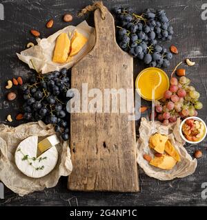Empty wooden vintage cutting board in center of frame made of honey grapes cheese snack other ingredients gastronomy snacks. Mock up copy space or Stock Photo