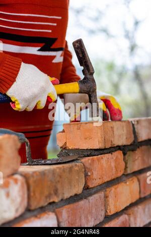 a man builds a brick wall, puts a brick on a cement-sand mortar, tapping a brick with a hammer Stock Photo