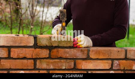a man builds a brick wall, puts a brick on a cement-sand mortar, tapping a brick with a hammer Stock Photo