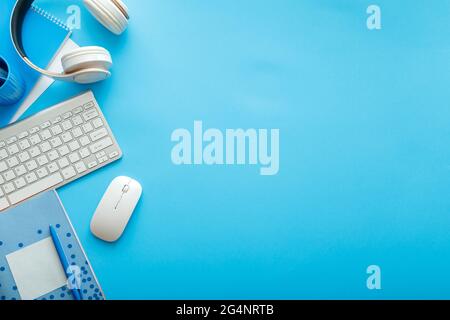 Computer desk with keyboard mouse headphones and notepad for paper work with copy space on Colored blue background. Work space desk for study or work Stock Photo