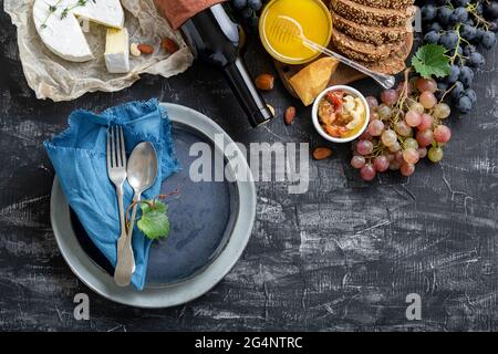 Empty serving blue plate with fork spoon in frame of food ingredients Mediterranean Kitchen. Blue plate dish in frame of food wine cheese on dark Stock Photo