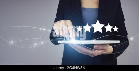 Hand pointing five star symbol to increase rating of company. White tablet in businesswoman hand with digital hologram Five stars 5 rating sign on gre Stock Photo