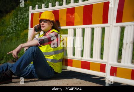 Male worker in hardhat and high vis jacket using smartphone. Stock Photo