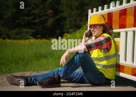 Male worker in hardhat and high vis jacket using smartphone. Stock Photo