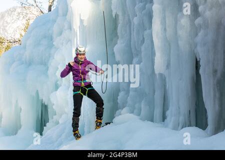 Woman ice climber tying a rope to his harness, preparing for a climb Stock Photo