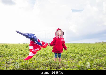 Patriotic Holiday. cute little child girl with American flag. USA celebrate 4th of July enjoying sunset on nature. Independence Day concept. Stock Photo