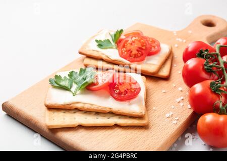 Board with tasty crackers and tomatoes on grey background, closeup Stock Photo